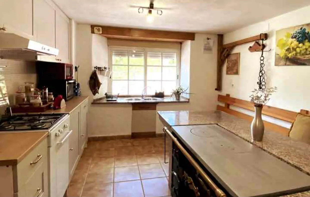 Cocina de la casa, con fogones de gas y mesa junto a la ventana